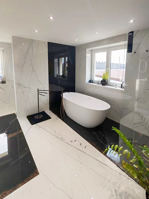 Salle de bain luxueuse avec baignoire îlot blanche ovale, revêtements en marbre blanc veiné et marbre noir