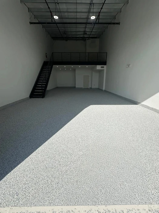 Espace industriel vide avec mezzanine, escalier métallique noir, plafond technique apparent